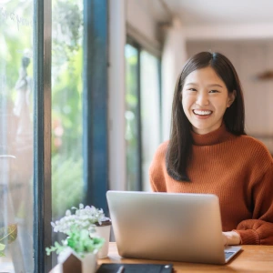 Smiling woman using a laptop in a cozy café, representing confidence in learning how to invest