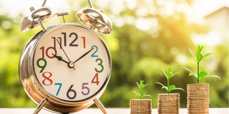 Alarm clock next to stacked coins growing into plants, symbolizing compound growth over time